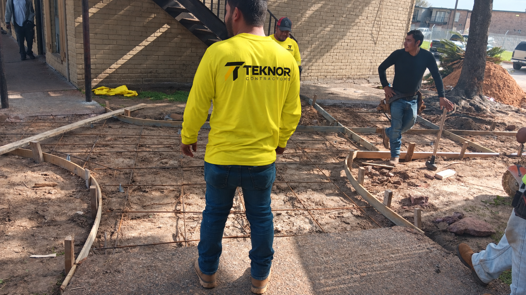 Workers coordinating concrete formwork and reinforcement on site; workwear branding digitally edited